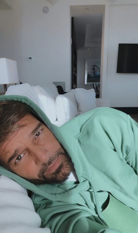 Ricky Martin on a white sofa in a green hoodie