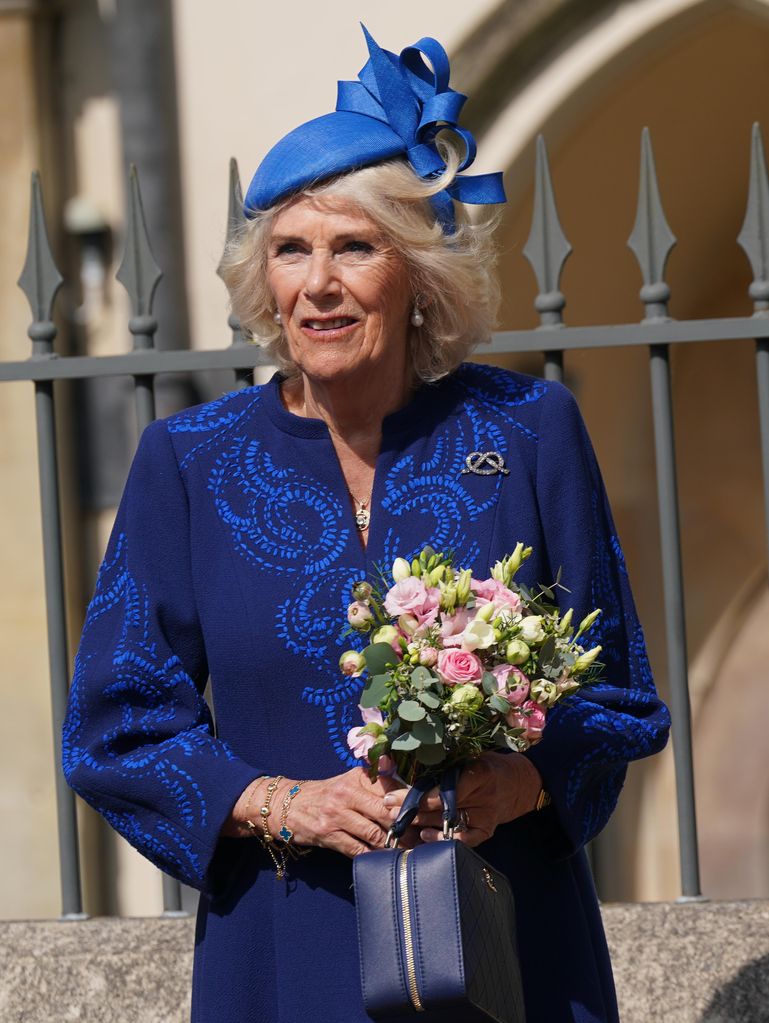 Queen Consort Camilla looking serious in a blue outfit holding a bunch of flowers