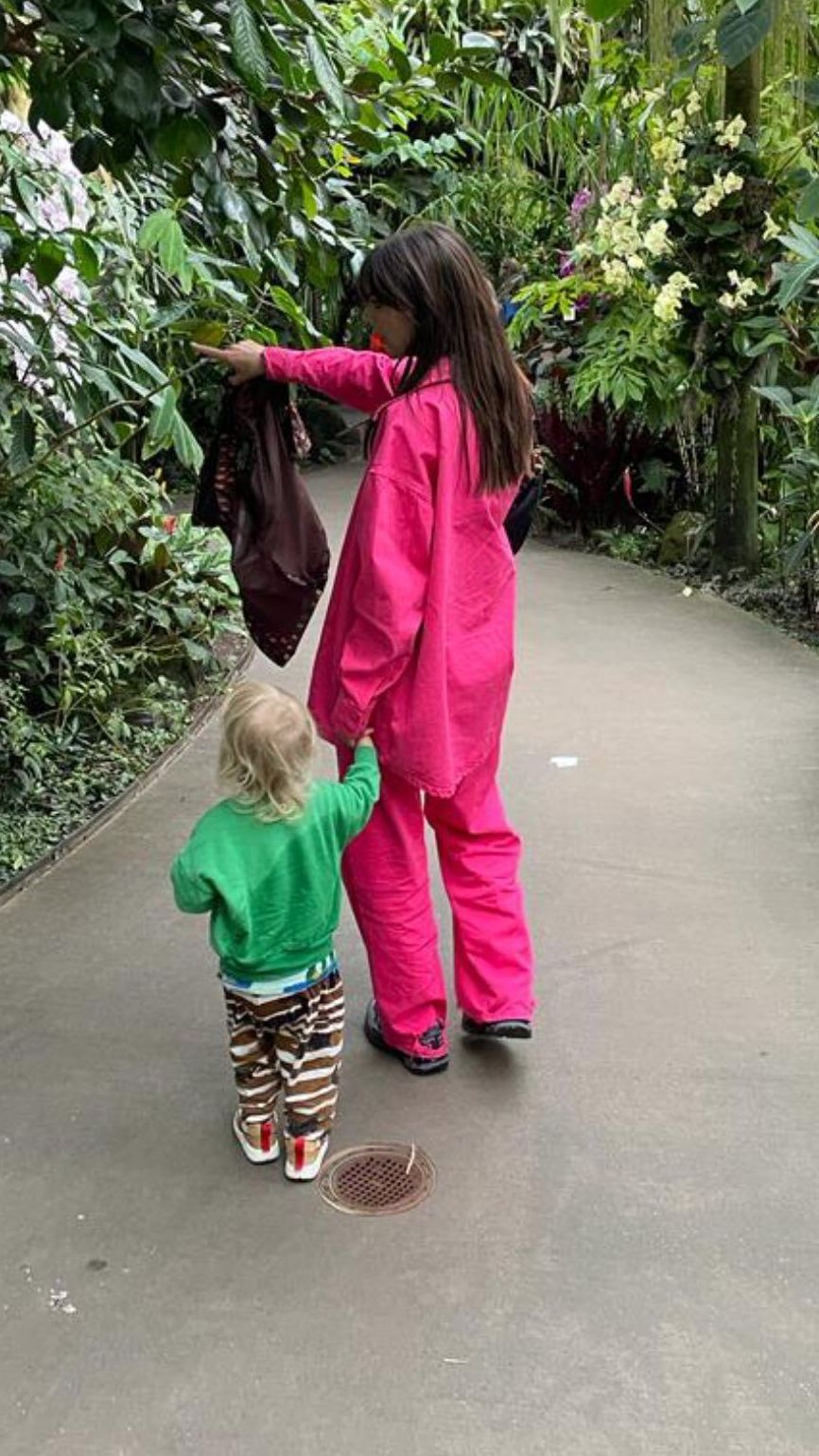 Emily Ratajkowski wearing a pink two piece in a park holding hands with her son