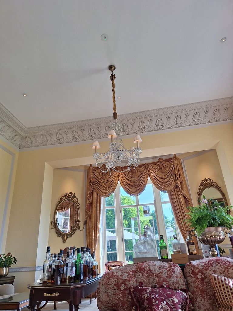 A room with a chandelier, bottles of alcohol, mirrors and sofas