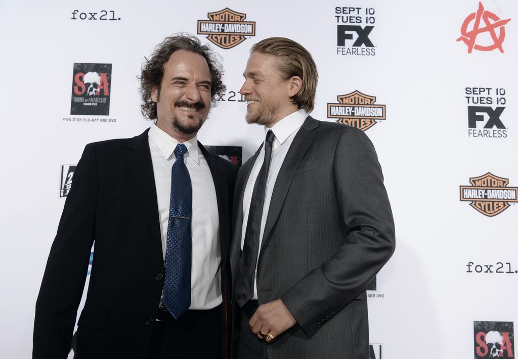 Charlie Hunnam regarde Kim Coates et passe un bras autour de son dos. Kim Coates sourit à la caméra.