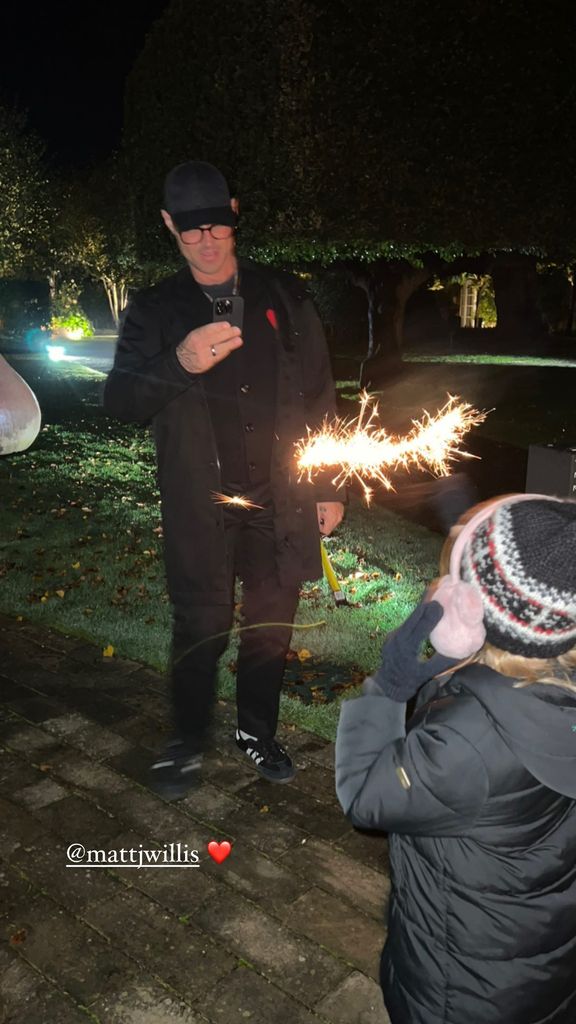 Matt Willis taking a photo on his phone of his son holding up a sparkler