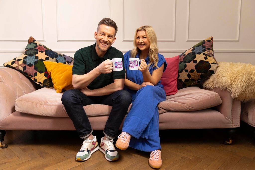 couple sat on velvet sofa holding mugs 