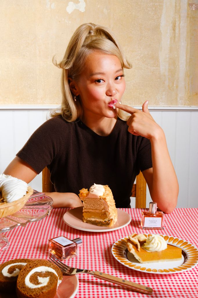 woman with plates of cakes in front of her sucking sweet treat from her finger 