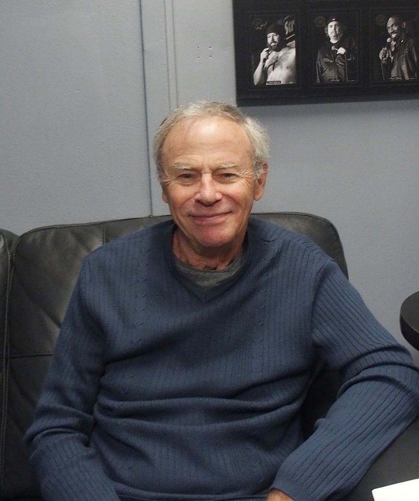 tristan rogers in blue sweater sitting on black chair