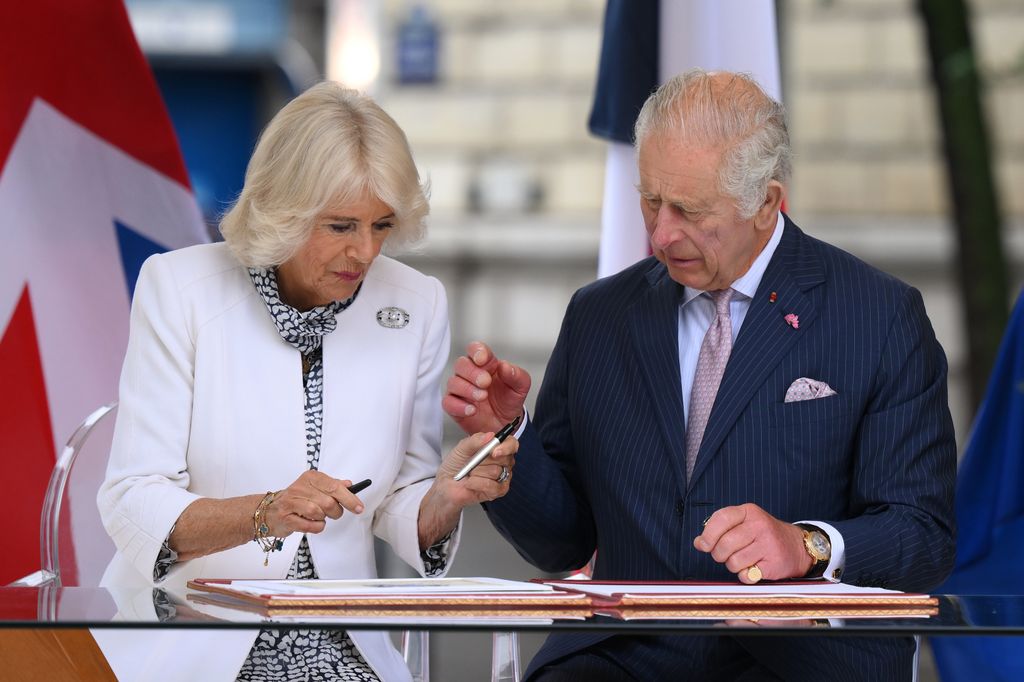 Queen Camilla and King Charles signing a book