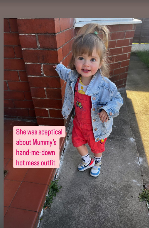 little girl in red dungarees standing outside house