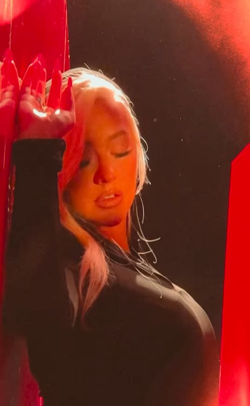 Christina Aguilera posing up against a wall in a black outfit