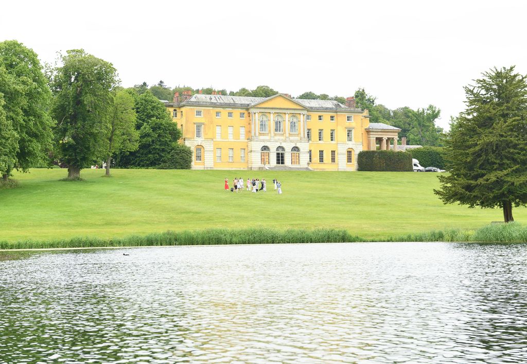 West Wycombe Park. The house in the distance is yellow surrounded by greenery. There is a lake in the foreground.