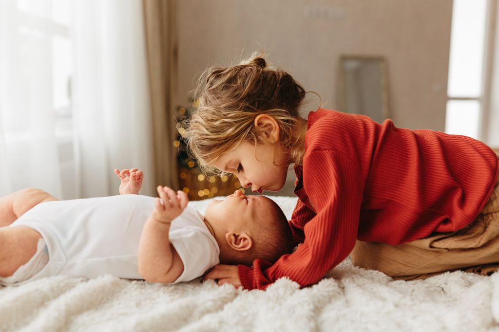 Adorable child kissing little sister lying on white bedding