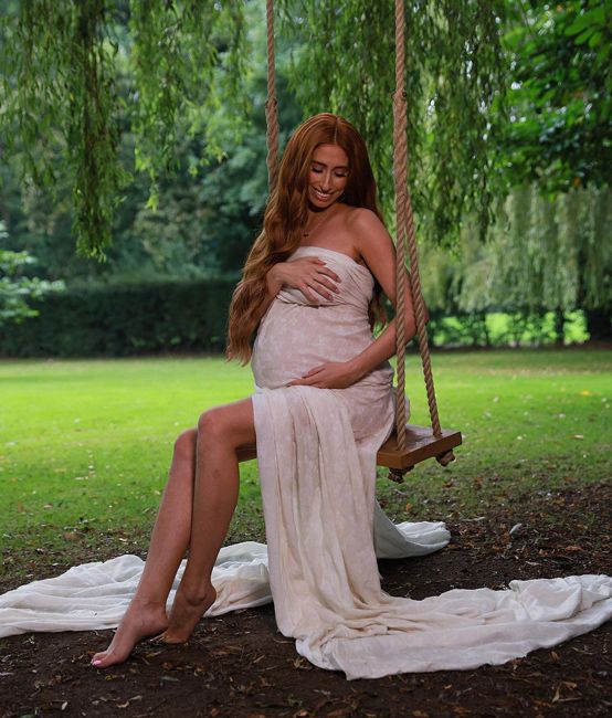 heavily pregnant stacey is swathed in semi sheer beige fabric as she sits on a swing under a willow tree and cradles her baby bump with a smile