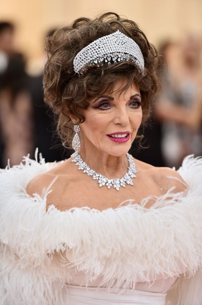 Joan Collins at the 2019 Met Gala in a white feathered gown, diamond tiara, necklace, and earrings.