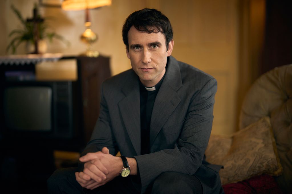 man in vicar's collar sitting in chair