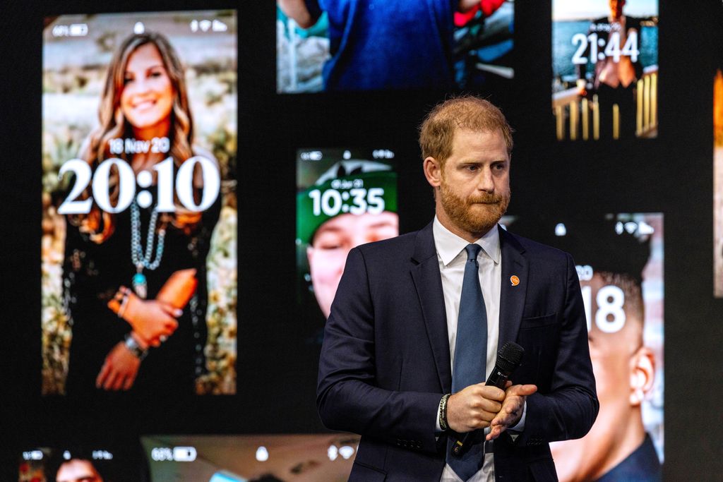 Prince Harry speaks on stage in front of pictures of phone lockscreens