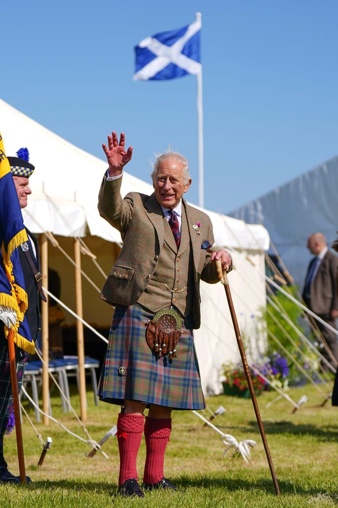 King Charles waving at people in front of the Scottish flag