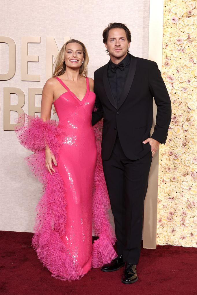 Margot Robbie in a pink dress with ruffles next to Tom Ackerley in a suit