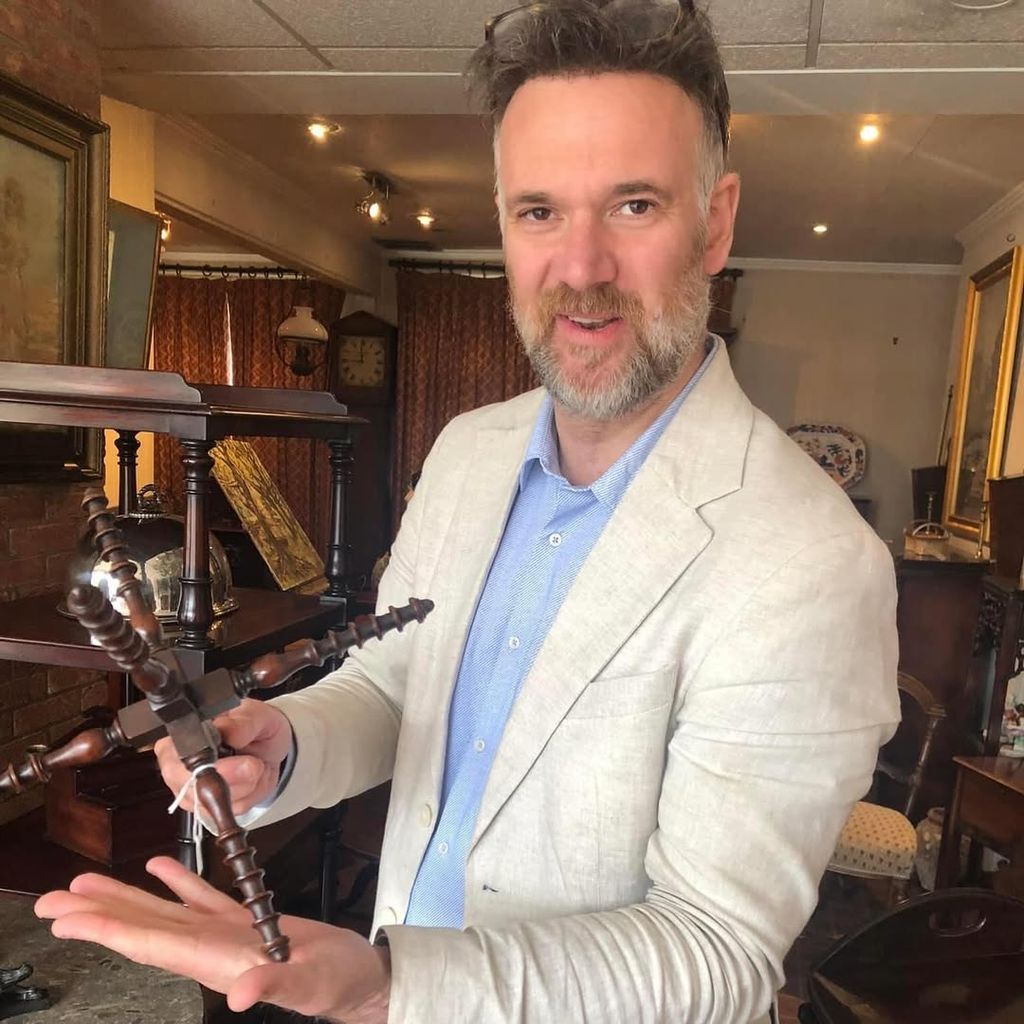 Charles Hanson in a cream suit and blue shirt proudly holding up a find from an auction
