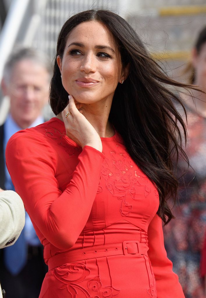 Meghan, Duchess of Sussex looking sideaways with windswept hair in red dress
