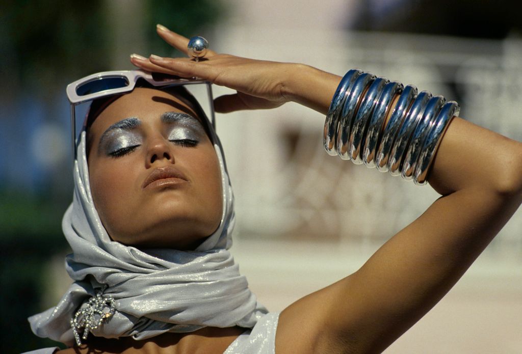 Model Yasmin Le Bon (aka Yasmin Paraneh) wearing a silver scarf by Zoran wrapped around head; sunglasses by Claude Montana for Alain Mikli; silver orbe ring, M & J Savitt; silver bangles