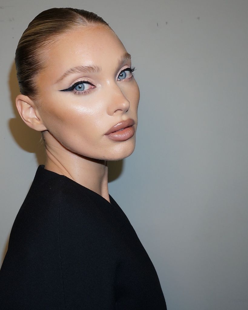 Elsa Hosk looks to the camera, her hair is slicked back into a bun, her makeup is radiant and dewy. She has a nude glossy finish on her lips and elongated black cat0eye liner. 