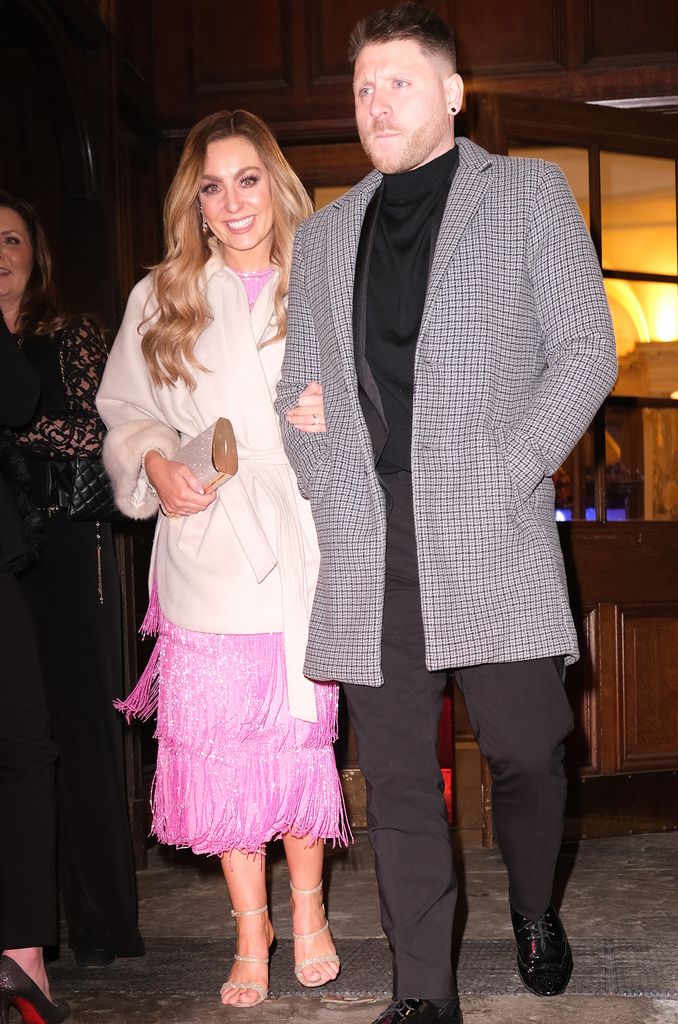 Amy Dowden in a pink dress and white coat arm in arm with her husband