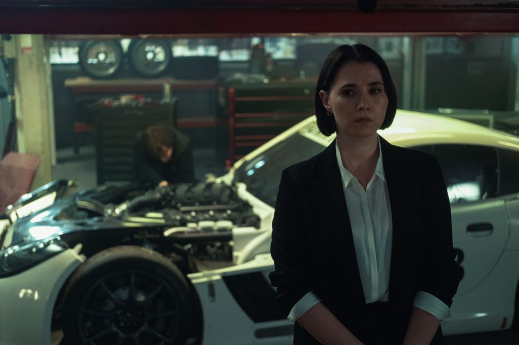 woman in shirt and blazer standing in dimly-lit car repair workshop