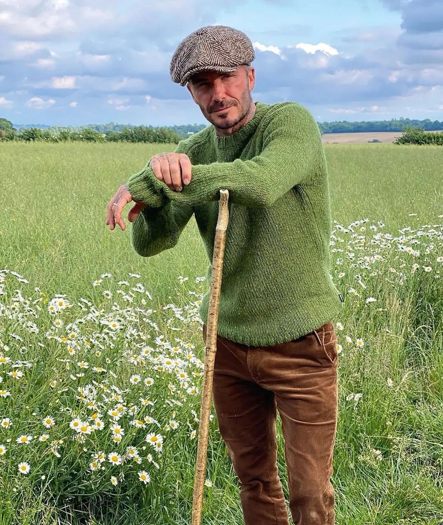 David Beckham wearing green jumper and flat cap standing in field