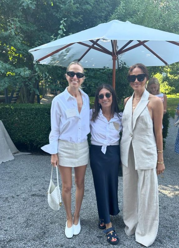 Two woman standing with Meghan Markle in a tan suit