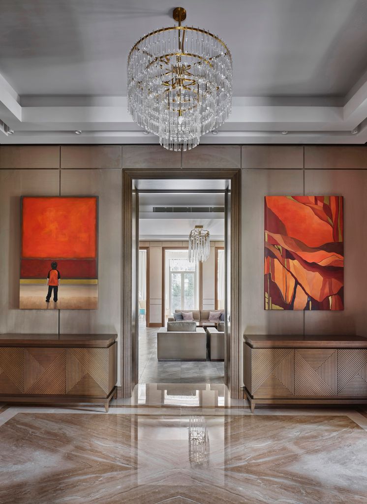 Interior design of a marble floored hallway with wood walls, a chandelier and orange artwork inside a mansion