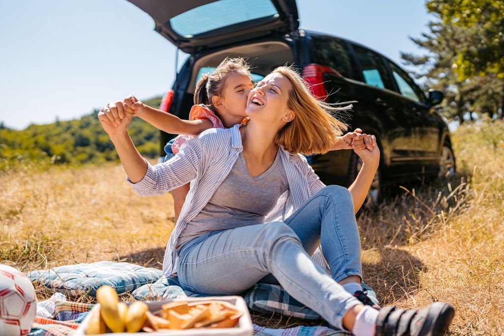Mid-Adult Woman And Her Elementary School Daughter Embracing While Having A Picnic In The Nature Outdoors