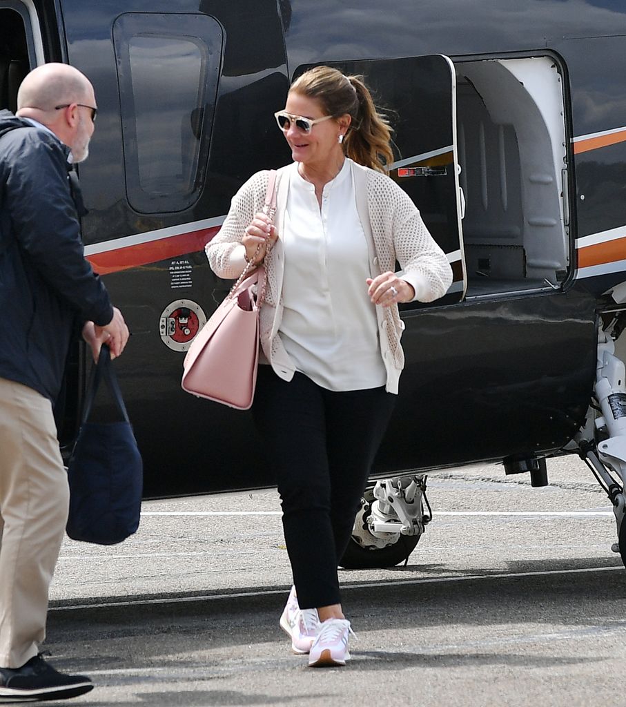 Melinda Gates is all smiles as she flashes a large ring while arriving to a heliport in New York City. Gates was met on the helipad by an assistant who helped with her bags. Melinda carried a pink Chanel bag and wore a mesh jacket, white blouse, black trousers, and Loewe sneakers, April 20, 2024