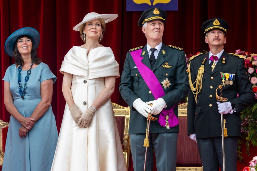 Queen Mathilde in a cream outfit and King Philippe in military uniform - both look concerned