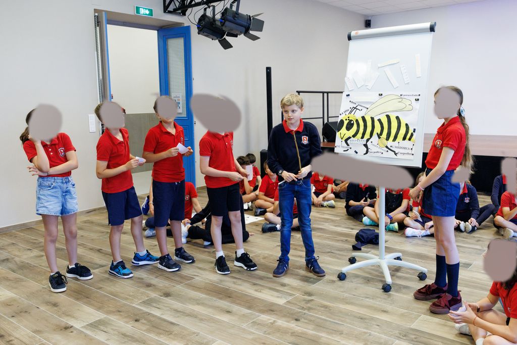Prince Jacques and a group of children standing by a board with a drawing of a bee