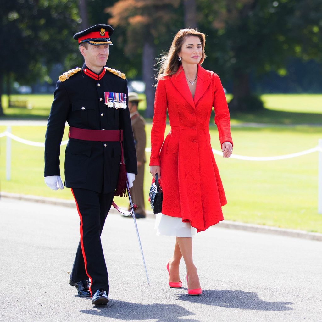 Queen Rania of Jordan in red dress beside army officer