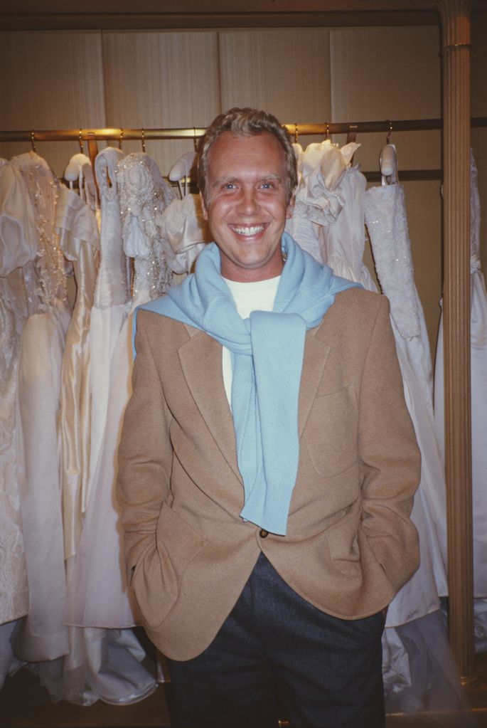 Michael Kors in a beige suit in front of a rack of wedding dresses