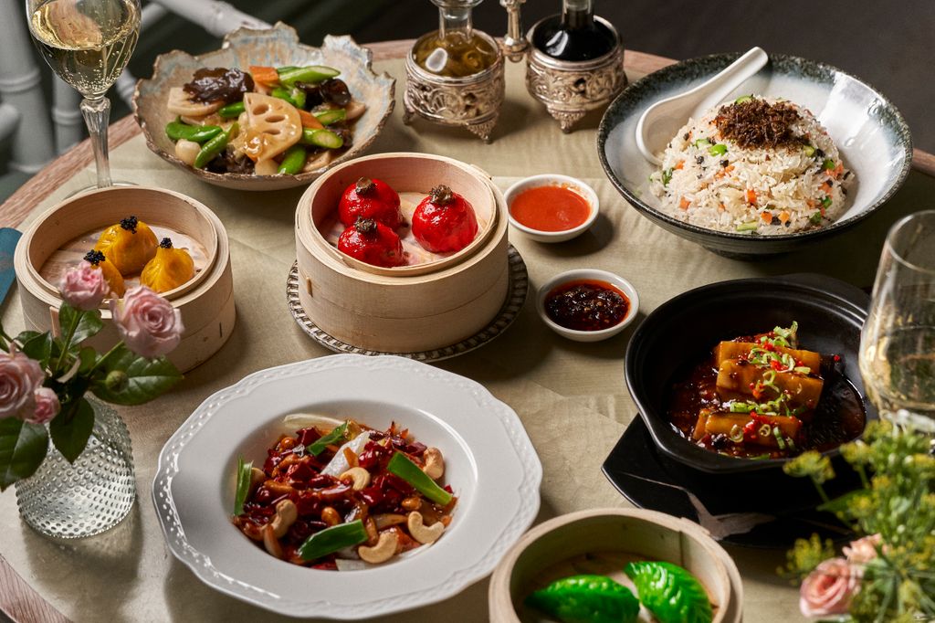 7 plates of Chinese food on a table, including dipping sauces and fresh pink flowers                  