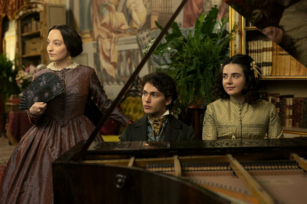 Three young people in period costume by piano