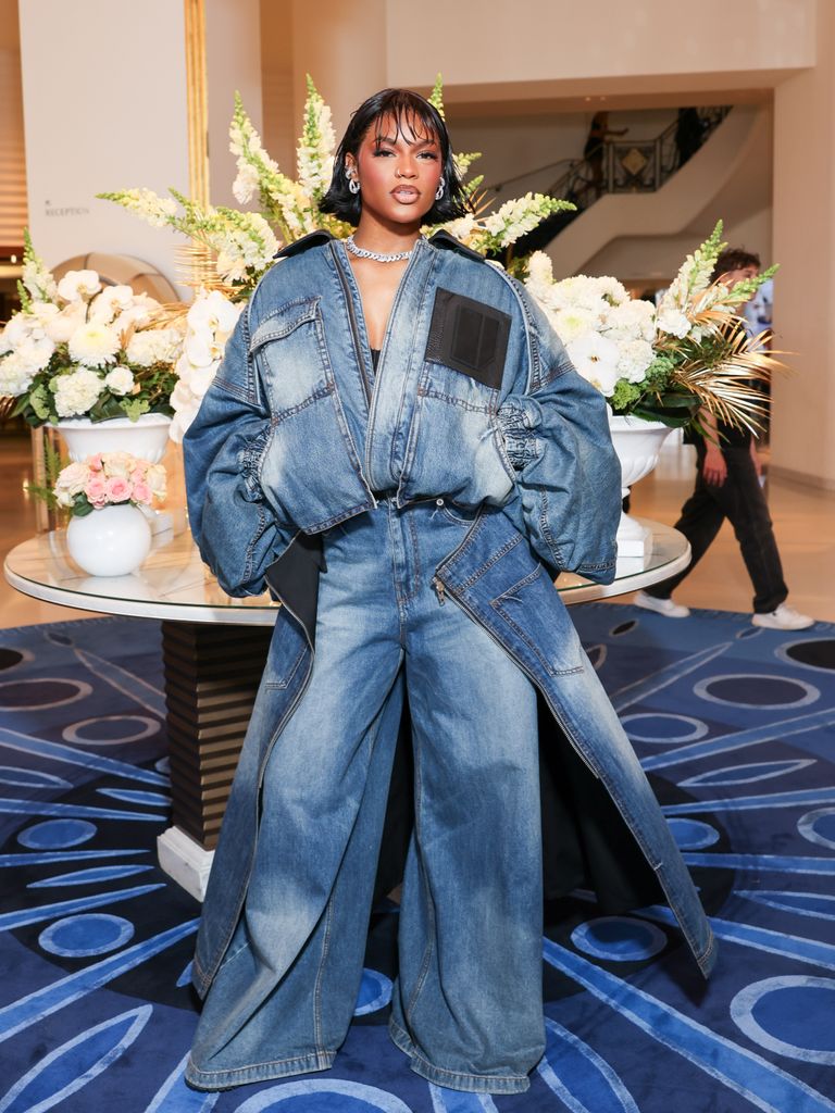 Didi Stone wears an oversized denim jacket and jeans with a denim skirt attached to the back half of the outfit