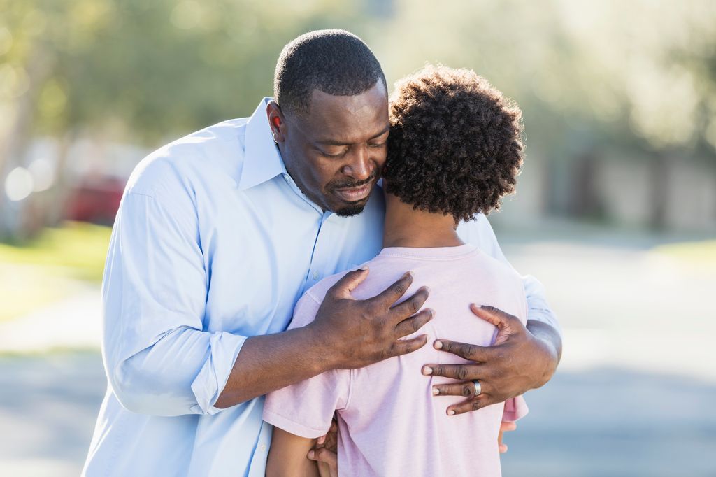 man hugging his teenage son, consoling him.