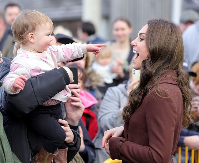 kate middleton in brown coat laughing as baby girl points at her