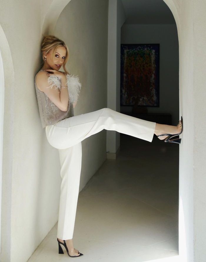 Kylie Minogue in white trousers with leg resting on wall