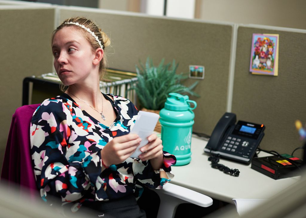 A woman sits at a desk holding paper