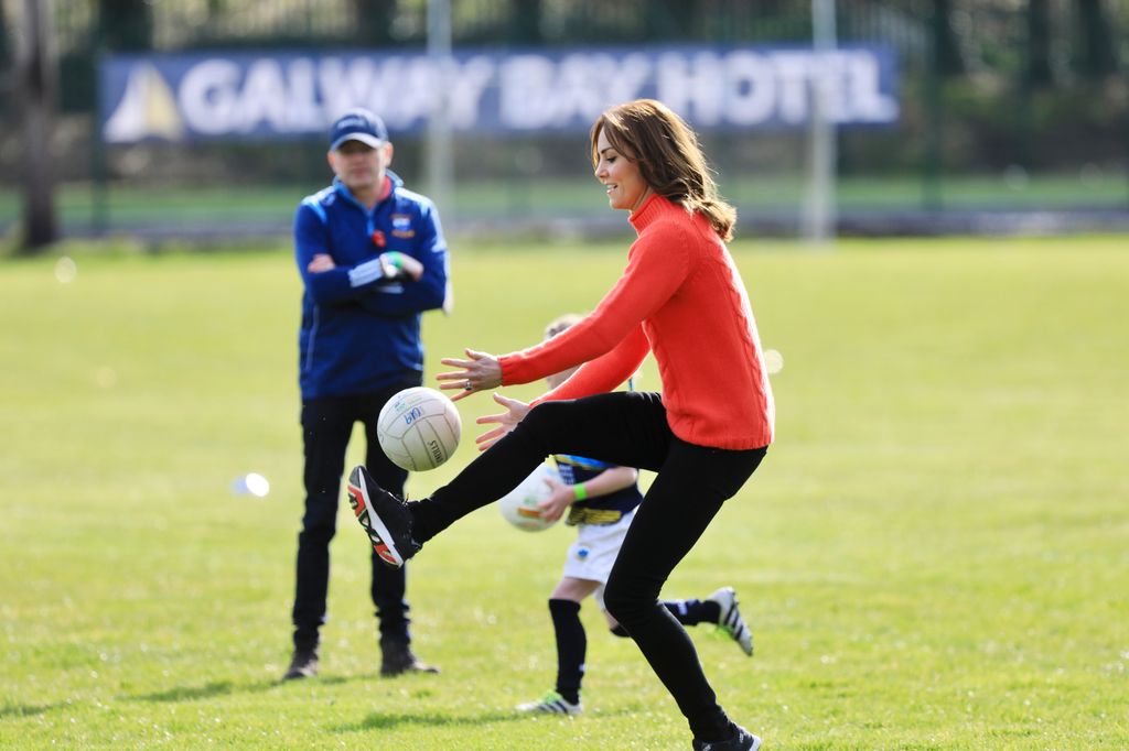Princess Kate kicking a ball in a red jumper