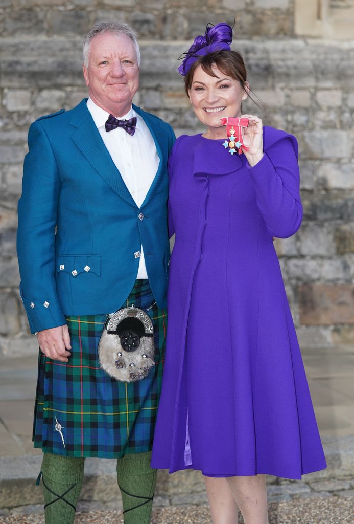 Lorraine Kelly in a purple dress with husband Steve Smith in a blue suit jacket and tartan kilt