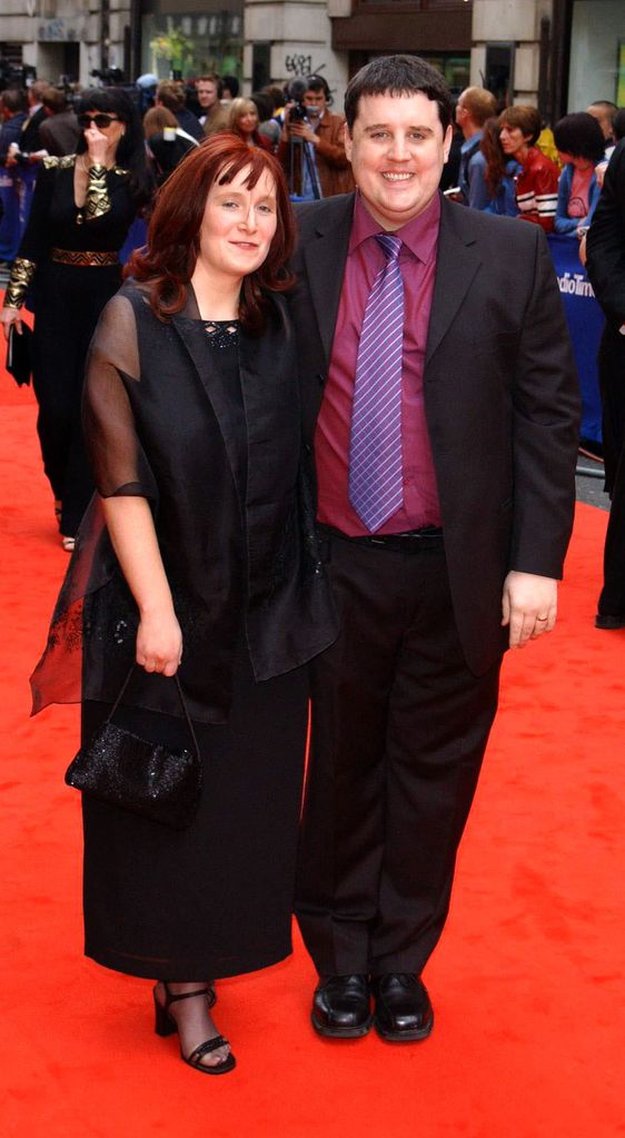 Comedian Peter Kay in a maroon shirt and suit on the red carpet with his wife Susan
