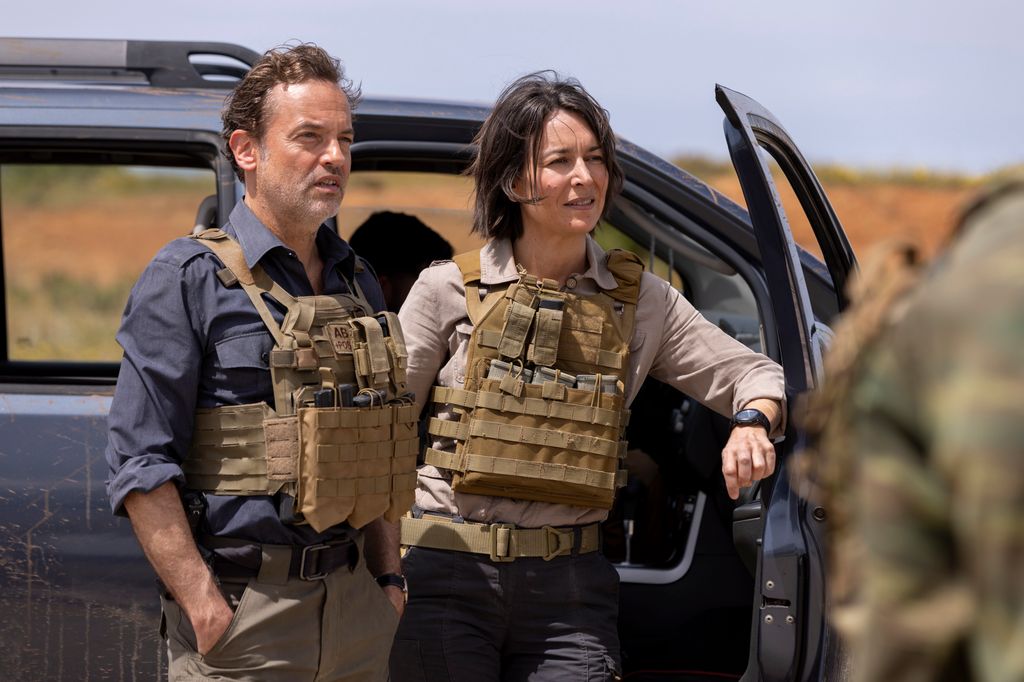 man and woman standing by car wearing protective vests