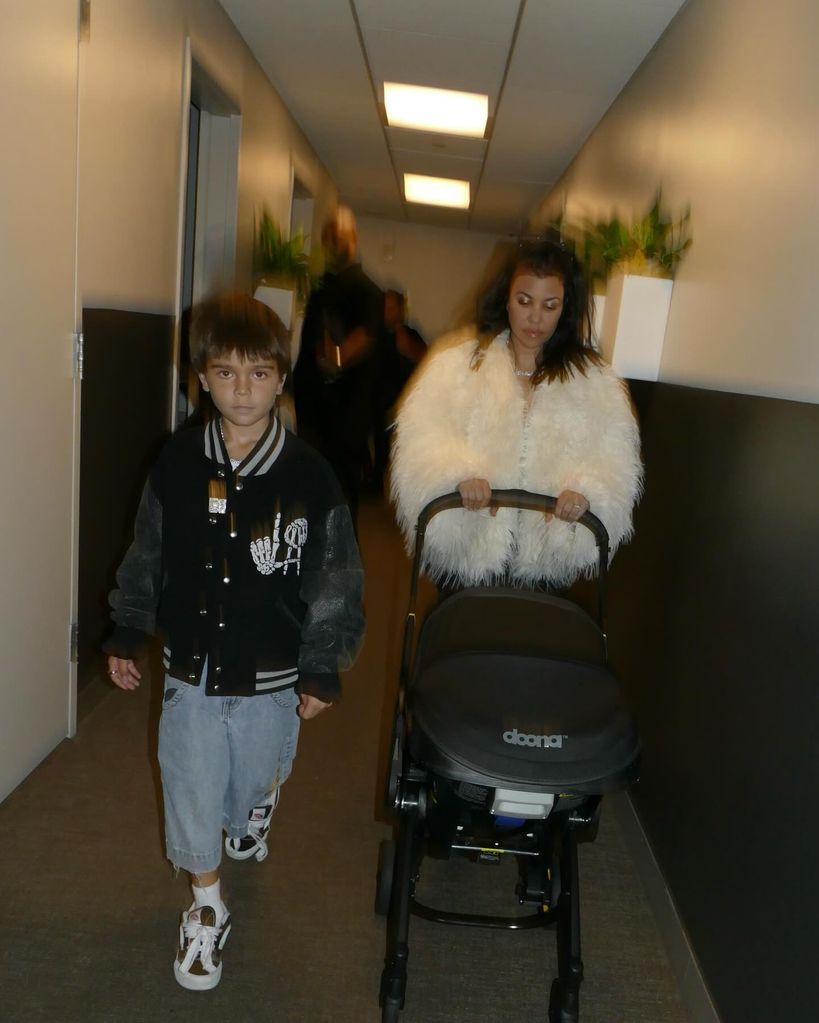 Reign Disick and Kourtney Kardashian walking down a corridor with Kourtney pushing a pram