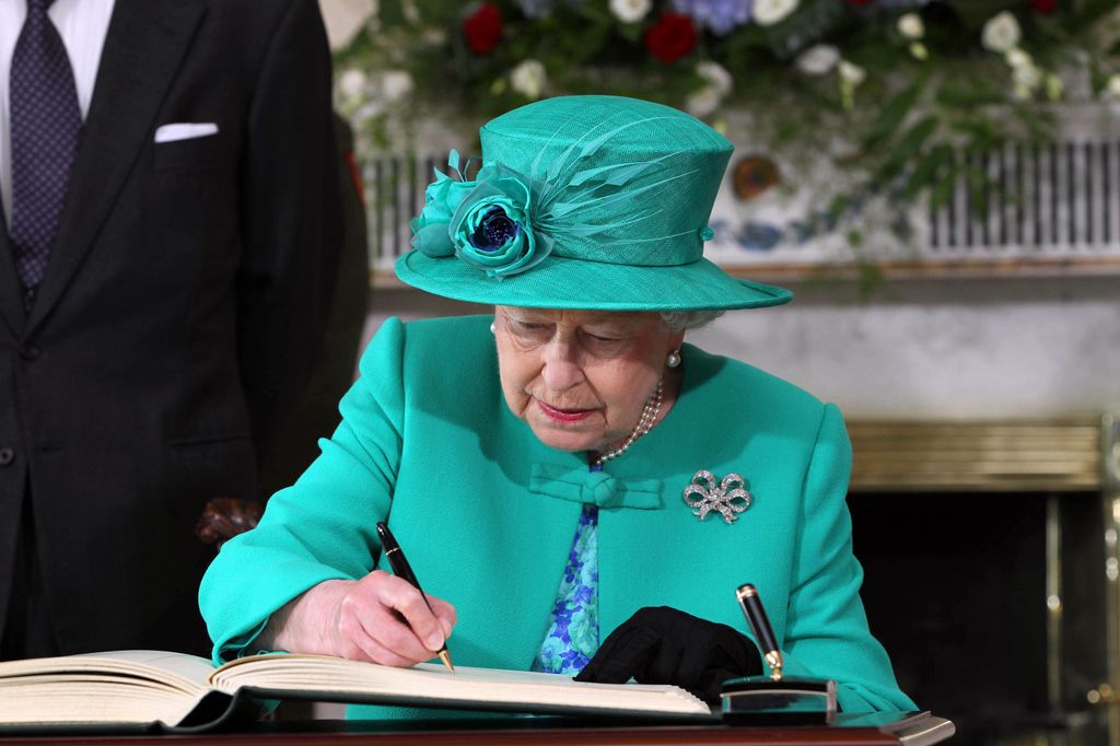 queen in green outfit signing a book