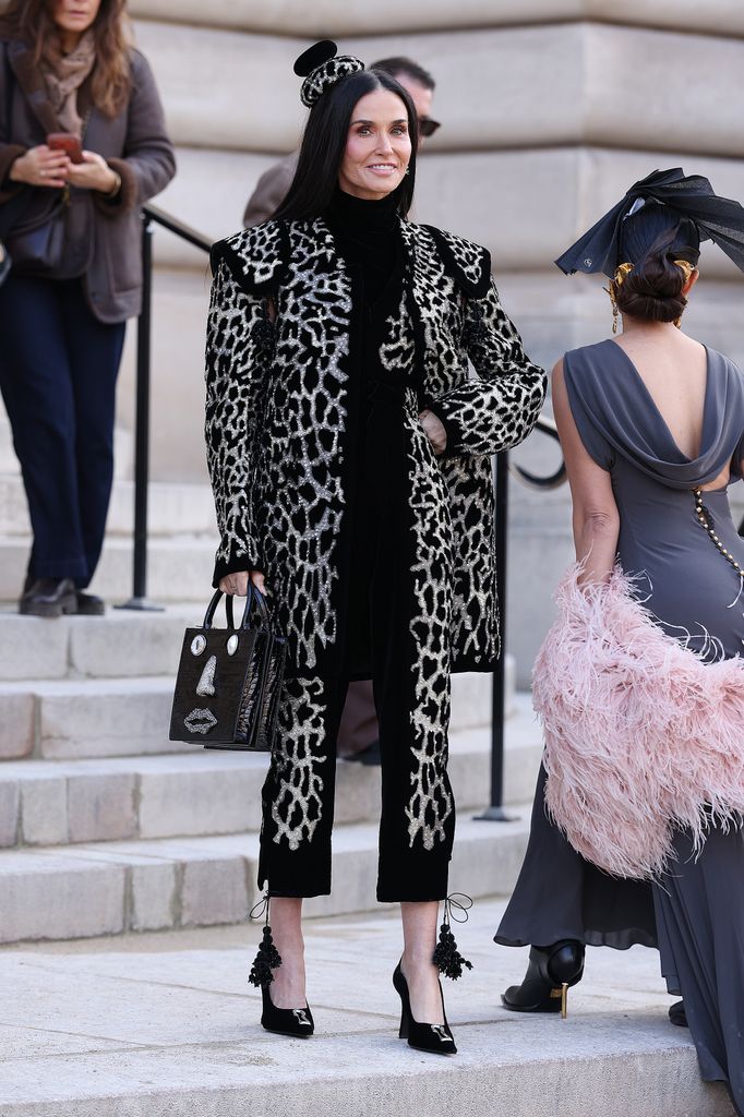 Demi Moore wears a giraffe print coat and black heels with a black Schiaparelli handbag