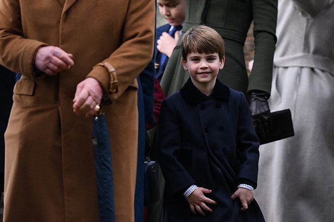prince louis smiles as he walks behind king charles